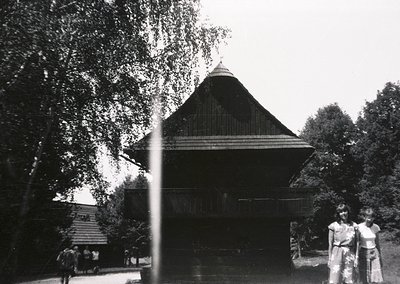Traditional wooden pavilion with steep gabled roof, surrounded by lush greenery. Mid-20th century architectural style, likely...