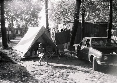 Mid-century camping scene with vintage tent and classic car. Child in shorts and shirt stands near a canvas tent pitched on a...