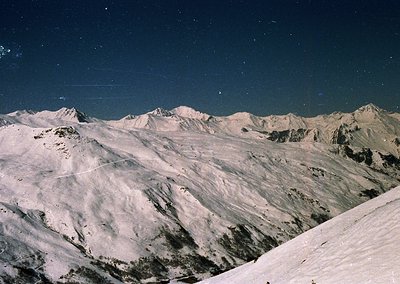 Stark alpine peaks under a star-studded night sky, showcasing jagged ridges and snow-covered slopes. The contrast of light an...