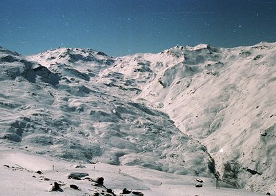 Snow-covered alpine peaks with rugged, undulating terrain under clear skies.
