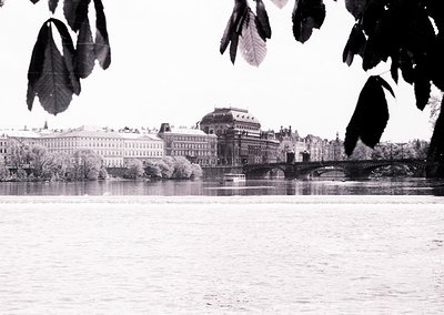 Mid-20th century urban riverscape: grand neoclassical buildings flank a bridge over calm water, framed by autumn leaves. Like...