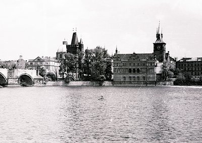Historic black-and-white view of Prague’s Vltava River featuring the Old Town Bridge Tower and Charles Bridge arches. Mid-20t...