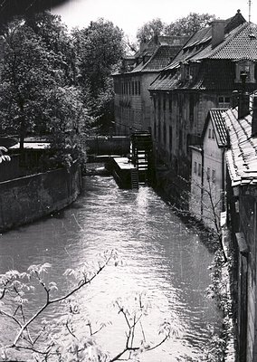 Historic waterwheel along a narrow canal flanked by timber-framed buildings with steeply pitched roofs, likely European . Sto...