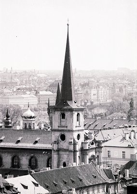 Prominent Gothic Revival church spire dominates Prague’s historic skyline, framed by Baroque-style rooftops below. Mid-19th c...