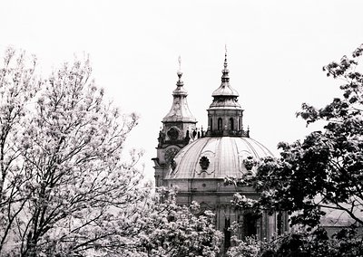 Baroque-style church dome with twin spires framed by leafless trees, suggesting winter or early spring. Ornate facade feature...