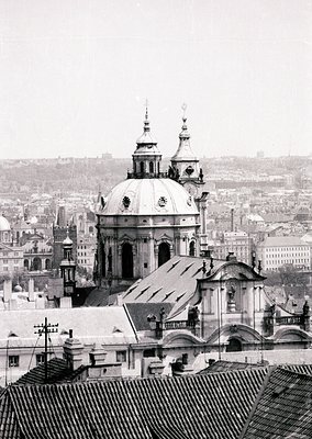 Baroque-style dome with twin spires dominates rooftops of a densely built European cityscape. Snow covers rooftops, indicatin...
