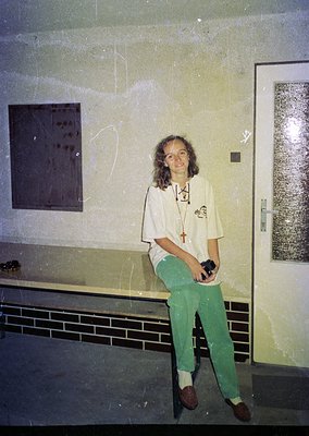 Indoor portrait of a person in a utilitarian space, likely a 1970s–1980s institutional or medical setting. The individual wea...