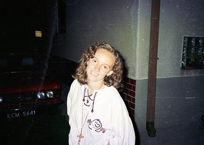 Vintage candid of a person in a 1980s-style hooded sweatshirt with cartoon graphics, standing beside a red classic car (KCM 5...