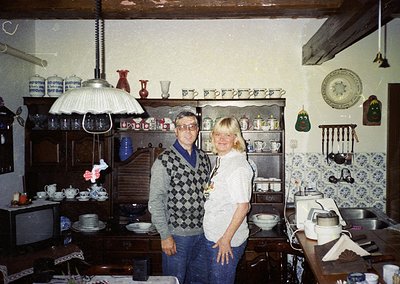 Vintage kitchen interior featuring wooden cabinets, blue-and-white patterned tiles, and ceramic dishes. Two individuals pose ...