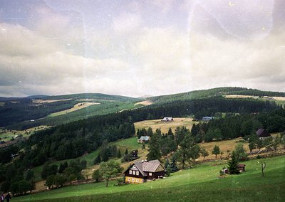 Vintage aerial view of a rural valley with scattered farmhouses, orchards, and forested hills under overcast skies. Likely Ea...