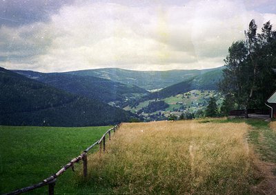Vintage-style landscape shot of rolling hills and valleys with misty, layered clouds. Rustic wooden fence in foreground, fram...