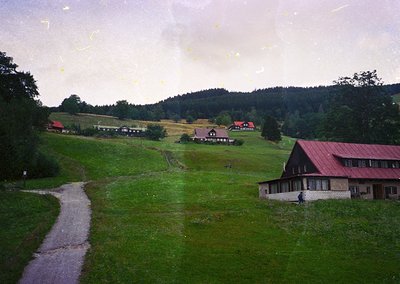 Vintage rural landscape featuring a winding gravel road leading through lush green meadows. Mid-20th century farmhouses with ...