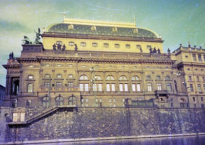 Grand neoclassical theater façade with ornate bronze statues, arched windows, and a domed roof. Architectural details suggest...