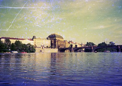 Vintage sepia-toned photograph of Prague’s **Charles Bridge** with **St. Nicholas Church** in background. Reflective water ca...