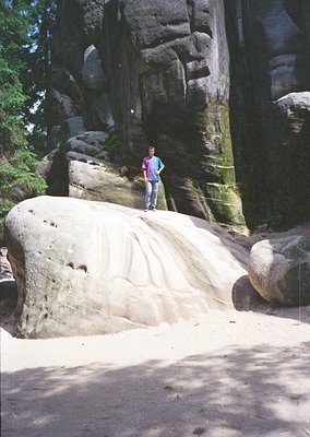 A person stands on a smooth, rounded boulder in a rocky canyon, surrounded by towering sandstone formations. The scene captur...