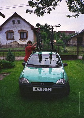 Green hatchback (likely a Renault Twingo) with roof-mounted bike rack carrying two bicycles, parked on grassy residential law...