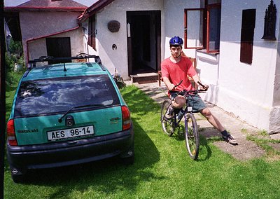 Vintage 1990s-era hatchback (AES 96-14) parked beside a residential building with a man in a red polo shirt riding a mountain...