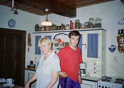 Vintage kitchen interior with two individuals posing near retro cabinetry and spice jars. Blue-and-white checkered cabinets c...