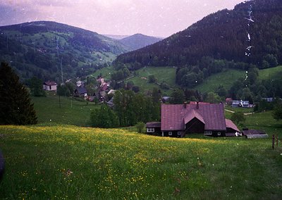 Vintage alpine village nestled in rolling green hills, featuring a prominent red-roofed chalet-style house in foreground. Sca...