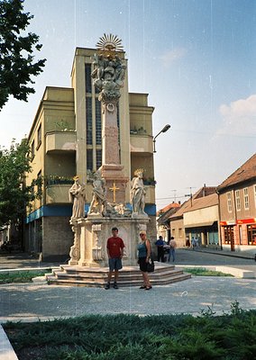 Ornate 19th-century monument featuring sculpted figures, a central cross, and a sunburst emblem atop a tall column in a Europ...