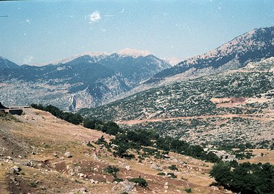 Rural mountainous landscape with sparse vegetation, winding road, and rocky terrain under clear skies. Likely Mediterranean o...