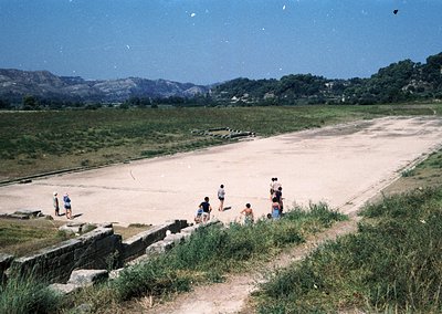 Vintage coastal scene with a group of people exploring ancient ruins by a shallow, sunlit inlet. Stone walls and remnants of ...