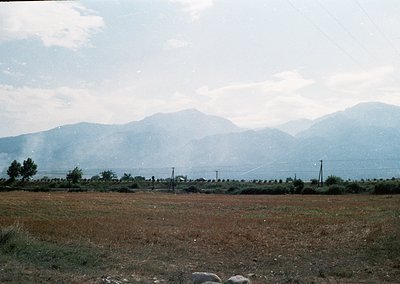 Vintage landscape shot of rural terrain with distant mountain range under hazy sky. Foreground features dry, cultivated field...