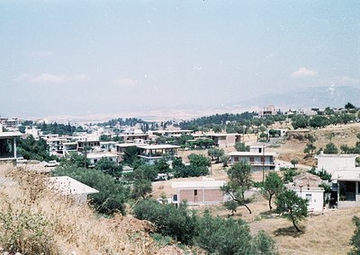 Aerial view of a mid-20th-century hillside settlement with sparse, low-rise concrete buildings. Vegetation—olive trees and sh...