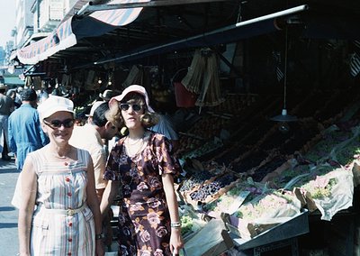 Vintage outdoor market scene featuring two women in 1960s-70s fashion: striped blouse with red buttons and wide-brimmed hat v...