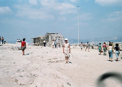 Vintage seaside scene with mid-20th-century beachgoers on rocky terrain. A partially constructed concrete structure (likely a...
