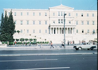 Neoclassical government building with prominent columns and symmetrical façade, likely the Greek Parliament in Athens. Pedest...