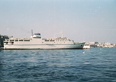 Mid-20th century ferry docked at port, likely Mediterranean. White hull with "Aegean" lettering, multiple decks, and lifeboat...