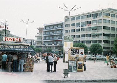 Vintage urban street scene featuring mid-20th century Thessaloniki, Greece. A Toyota dealership sign and "Tom Makedoniki" (au...
