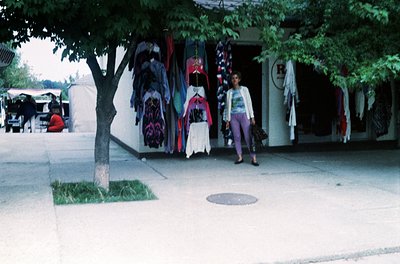 Vintage outdoor clothing stall with colorful, patterned garments hung on display. Woman in 1970s-style patterned top and wide...