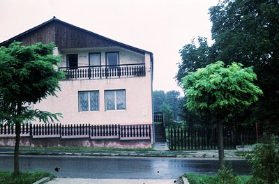 Two-story residential building with mid-century modern elements: cream-painted walls, dark wooden balcony railings, and a slo...