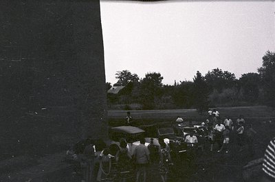 Vintage black-and-white photo of a mid-20th century outdoor gathering, likely a wedding or community event. Group of men in s...