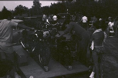 Vintage black-and-white photo of a motorcycle stunt act on a raised platform, featuring a rider in full leathers performing a...