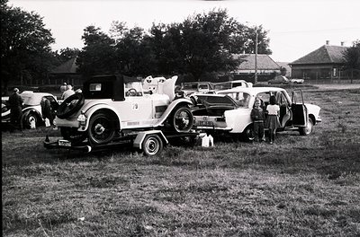 Vintage car show featuring classic automobiles, likely mid-20th century (1940s–1950s). Three open-top vehicles dominate: a wh...