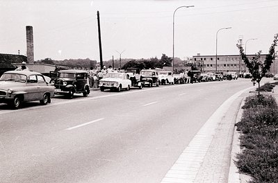 Mid-20th century urban street jammed with vintage cars, likely 1950s–1960s. Dense traffic of classic sedans, station wagons, ...