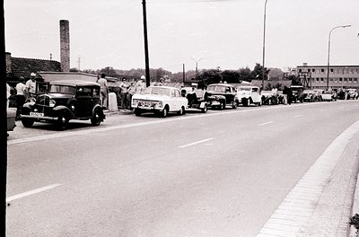 Vintage black-and-white street scene with mid-century cars, including a vintage sedan with visible license plate "5555" and a...