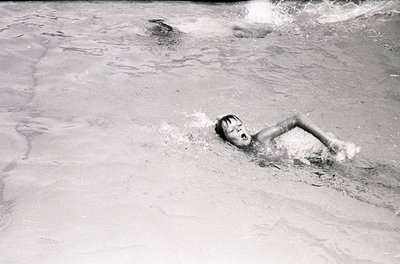 Black-and-white shot of a child mid-dive into shallow water, arms extended forward. Dynamic composition captures motion and y...