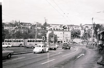 Mid-20th century urban intersection with vintage vehicles, including a classic bus and sedans, navigating a curved road. Over...