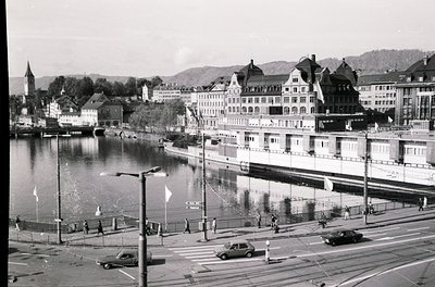 Historic lakeside urban scene featuring early 20th-century European architecture. Prominent multi-story buildings with ornate...