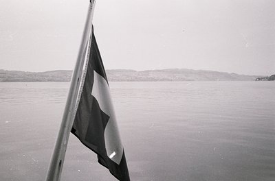 Black-and-white flag with red star and sickle on a pole, likely Soviet-era, over calm waters with distant hills. Mid-20th cen...