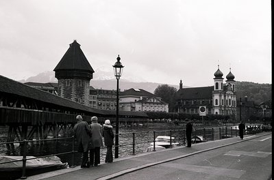 Black-and-white shot of the **Kapellbrücke (Chapel Bridge) in Lucerne, Switzerland**, featuring its iconic wooden bridge with...