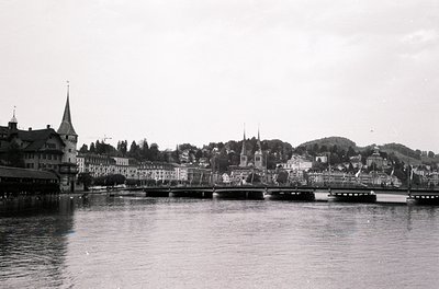 Black-and-white riverside cityscape featuring historic European architecture. Prominent spires, gabled roofs, and a bridge sp...