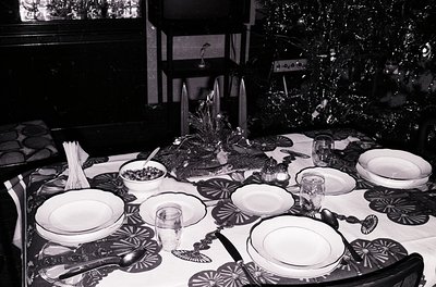 Elegant 1950s-60s holiday dining setup with symmetrical tableware: white plates, silverware, and glassware on a dark tableclo...