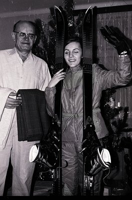 A man and woman pose indoors with alpine gear, likely in a ski shop or training facility. The man holds a pair of skis while ...