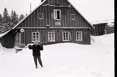 Black-and-white alpine lodge with wooden clapboard siding and white-framed windows, set in deep snow. A person in winter gear...