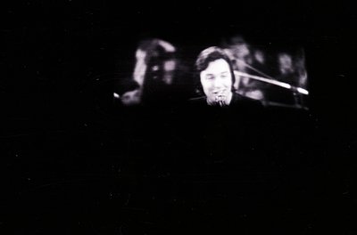 Blurred black-and-white close-up of a saxophonist performing live, captured with shallow depth of focus. The musician’s focus...
